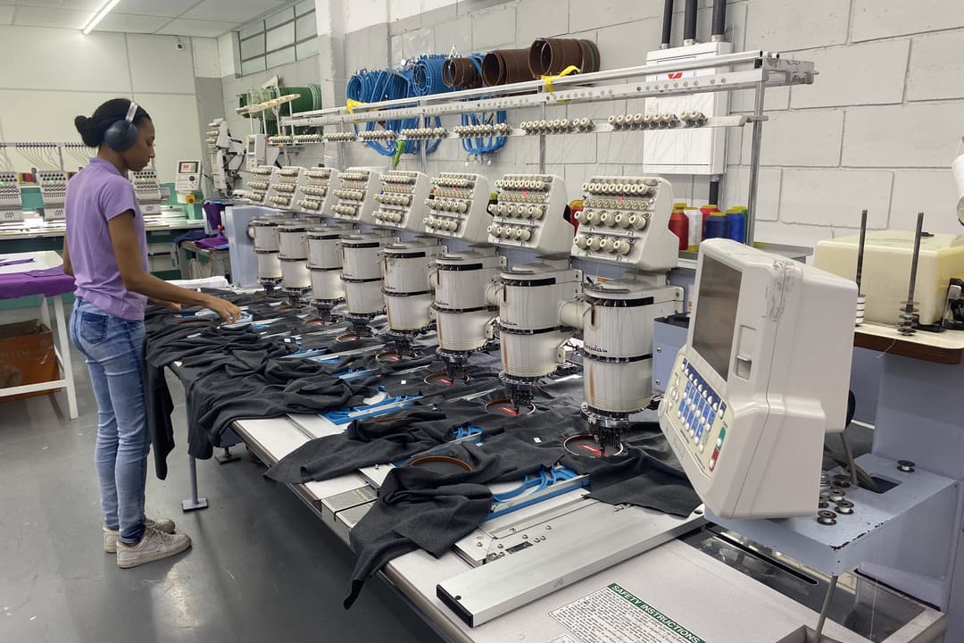 Profissional operando máquina de bordado industrial em processo de personalização de uniformes.
