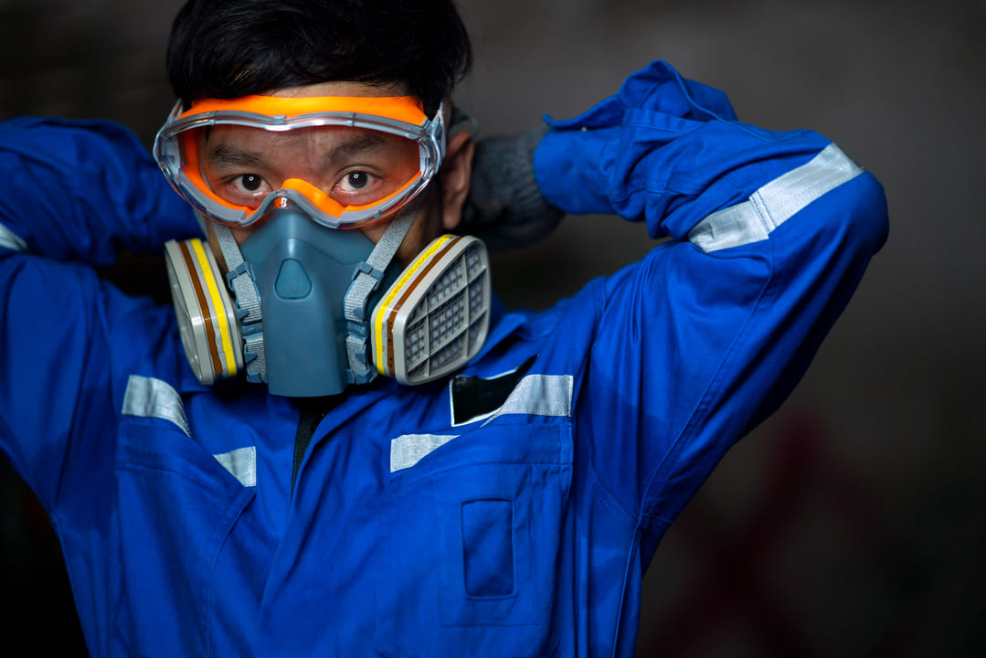 Trabalhador com uniforme azul e máscara de proteção respiratória com filtros, exemplificando o uso correto de EPI com Certificado de Aprovação (CA).