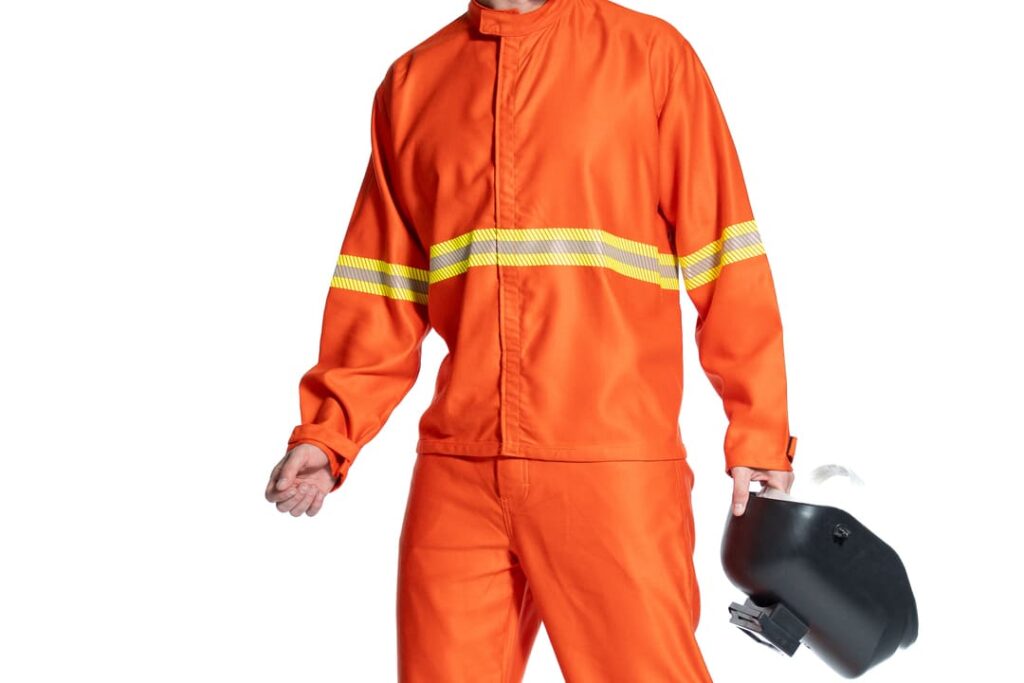 Pessoa vestindo uniforme de segurança na cor laranja com faixas refletivas amarelas, segurando um capacete de proteção preto em uma das mãos. A imagem tem fundo branco.